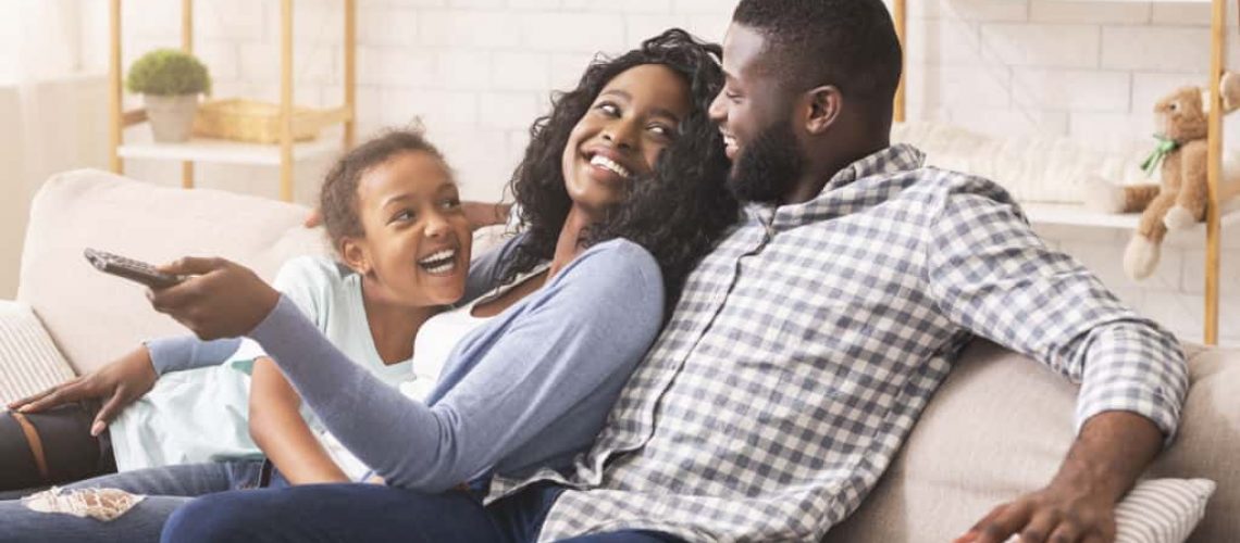 Joyful black family having fun together, relaxing on sofa at home.